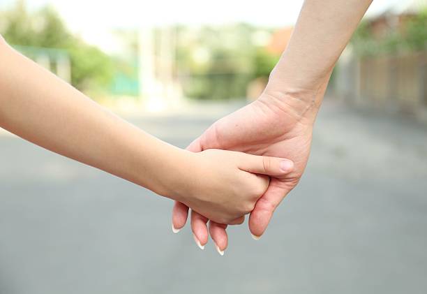 Mother and daughter holding hands outdoors, closeup