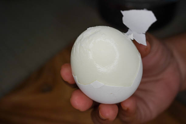 istock Woman peeling boiled egg at wooden table. Closeup and selective focus. 2212240622