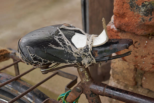 close-up of worn out and damaged black bicycle seat, frame is partly visible leaning against an old brick wall, aged and used seat with tears and cracks, soft focus with copy space