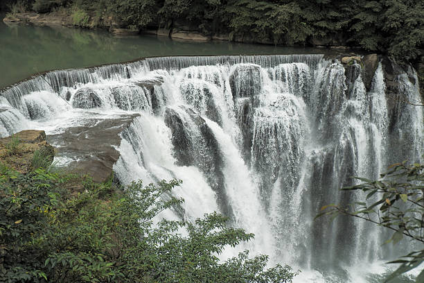 istock Powerful waterfall cascades over rocky cliffs surrounded by lush green forest and a calm river above. 2212245951