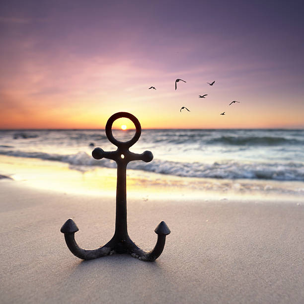 iron anchor in the sand on the beach in sunset light