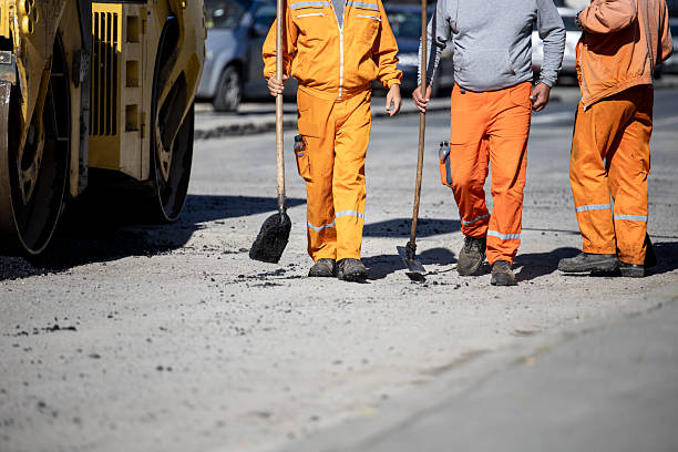 istock Road construction workers in bright orange uniforms performing asphalt repair on a sunny day 2212249230