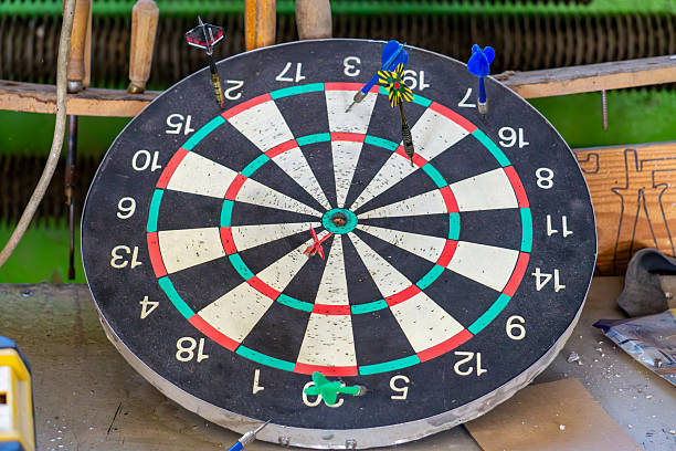 used dartboard with several darts stuck in it in different places. The dartboard is placed in a workshop environment
