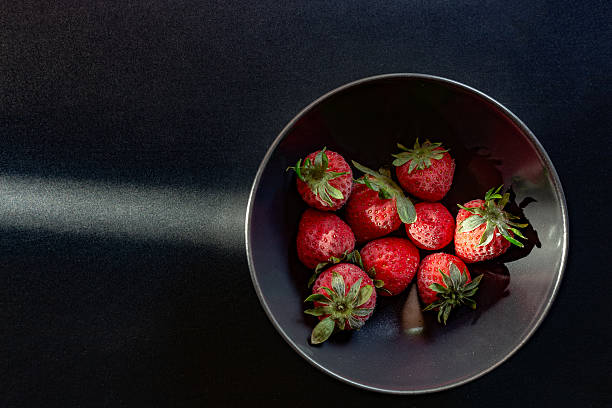 istock Fresh strawberries resting in a dark bowl on a black table 2212252378