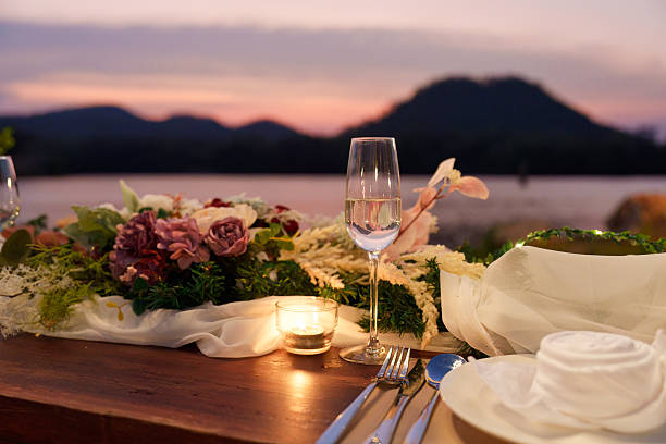 Rustic style wooden dining long table with flower, wine glass, candle decoration during dinner by the lake in the sunset