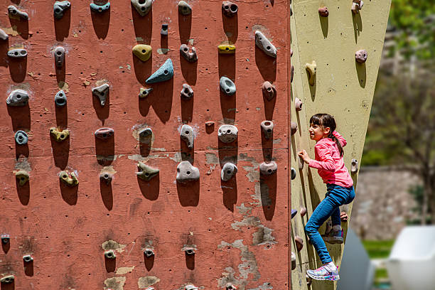 Smiling sporty little girl climbing artificial boulder on practical wall in gym