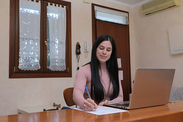 istock Young woman working from home, taking notes from her laptop 2212260906