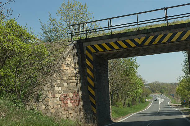 A stunning and picturesque view features a historic stone bridge gracefully arching over a roadway with warning markings
