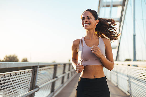 Woman jogging outdoors on a sunny day, wearing a fitness outfit, smiling confidently.