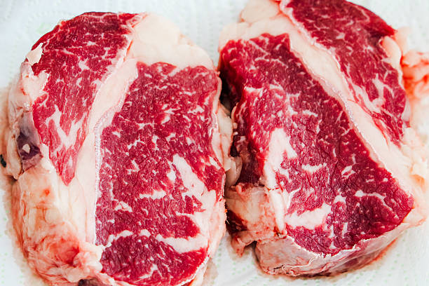 Two raw ribeye steaks display vibrant marbling and color waiting to be seasoned and grilled during a summer backyard barbecue.