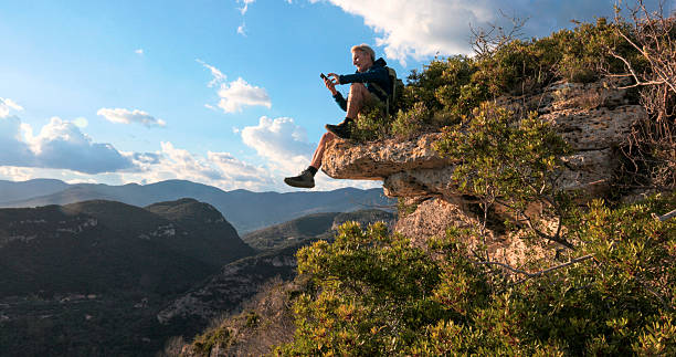 Hiker uses mobile phone on edge of mountain, Liguria
