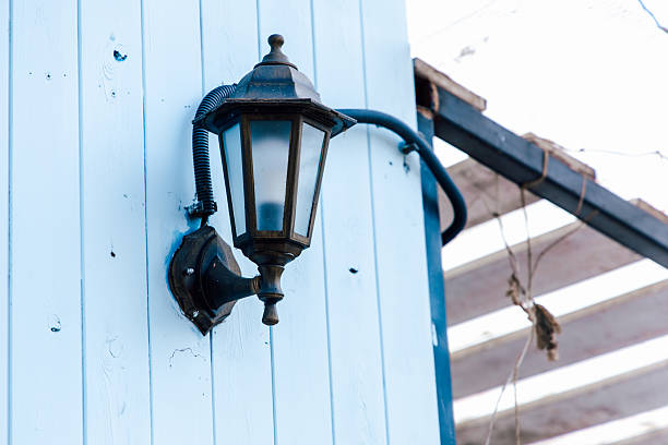 A vintage lantern is mounted on a blue wooden wall illuminating the area during the day. The structure shows signs of wear enhancing its charm.