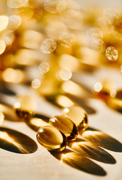 Close-up of golden capsules glowing under warm sunlight, casting soft shadows on a textured surface with an elegant bokeh effect.