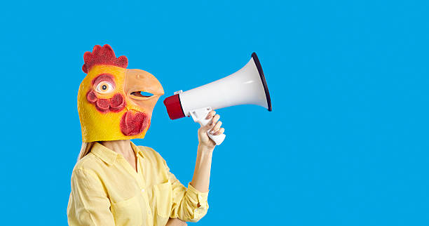 istock Female in rooster mask screaming into loudspeaker isolated on blue studio background 2212272247
