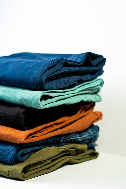 A close-up of neatly folded jeans stacked on a table at an outdoor market. Various shades of denim, from black to dark blue, are arranged in rows, creating a textured and organized display of casual clothing in a retail setting.