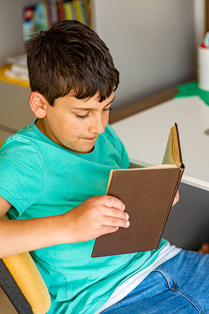 istock Boy reading a book on a chair 2212280606