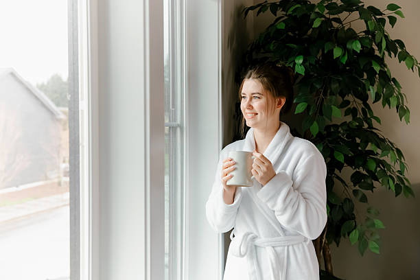 istock Woman in bathrobe looking out window at home 2212300154