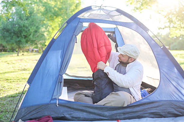 Young hispanic traveler pulls out a sleeping bag, sitting inside his blue tent while camping outdoors.