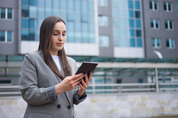 istock Young businesswoman using digital tablet while standing outside modern office building 2212304412