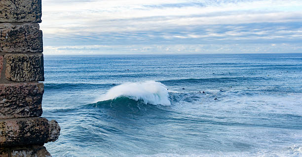 Dramatic ocean vista. A powerful wave crashes against the shore, seen through a stone structure. Evokes adventure and strength. Ideal for travel, nature, or resilience themes.