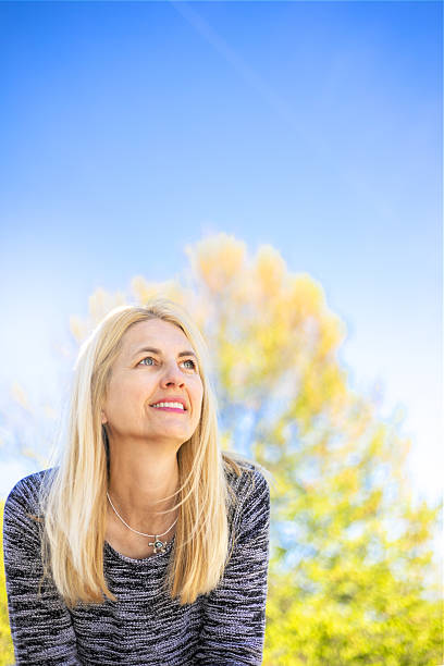 A young woman covers her face with a book while sitting on the grass with her head tilted back, resting from exhaustion.