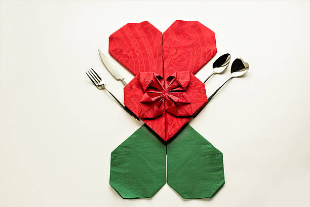 Three luxury paper napkins folded in heart shaped on the white background with cutlery