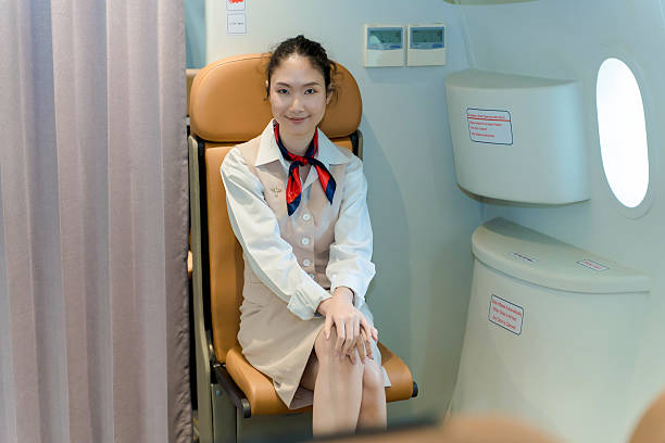 Smiling flight attendant seated on jumpseat with hands folded, ready for takeoff procedures inside passenger aircraft, showing calm and professional demeanor