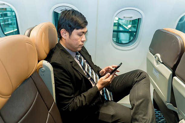 istock Businessman in formal suit using smartphone while seated by the airplane window, focused on screen during flight travel, modern in-flight connectivity concept 2212325567