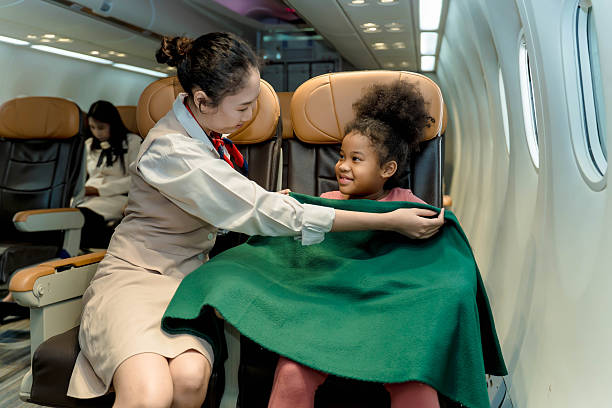 istock Flight attendant caring for a smiling child by wrapping her in a blanket during flight, showcasing airline comfort, safety, and exceptional in-flight service 2212325598