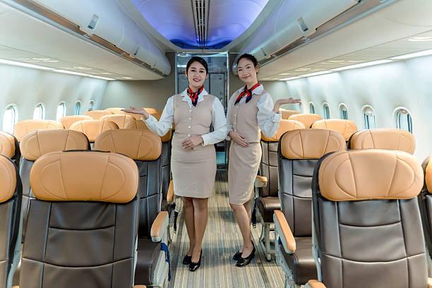 istock Smiling flight attendants standing in airplane aisle with welcoming gestures, showcasing hospitality and professional service inside commercial aircraft cabin 2212325636