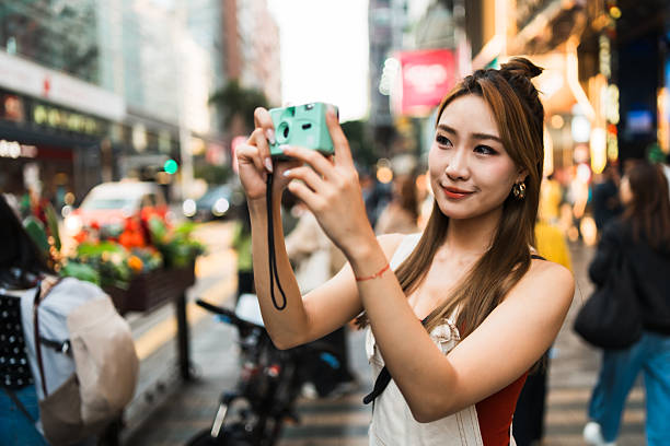 istock Young woman using retro camera in a busy street. 2212327102