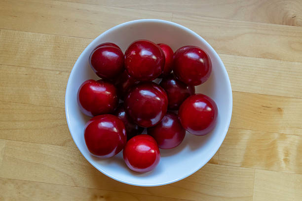 Red sour plums in a white ceramic bowl. Top view or flat lay.