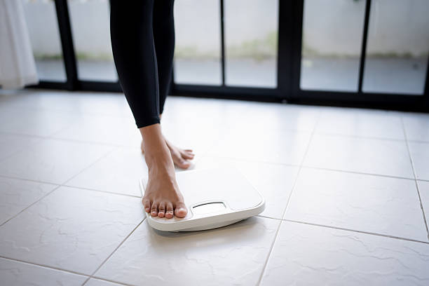 istock Lose weight. Fat diet and scale feet standing on electronic scales for weight control. Measurement instrument in kilogram for diet 2212330077