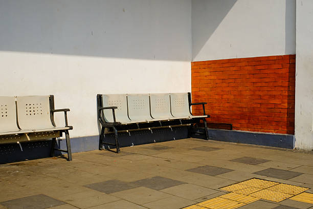 A contemporary metal bench sits along a pavement, enhancing the streetscape with its clean lines. Bright green accents from the nearby building add a pop of color to the setting.
