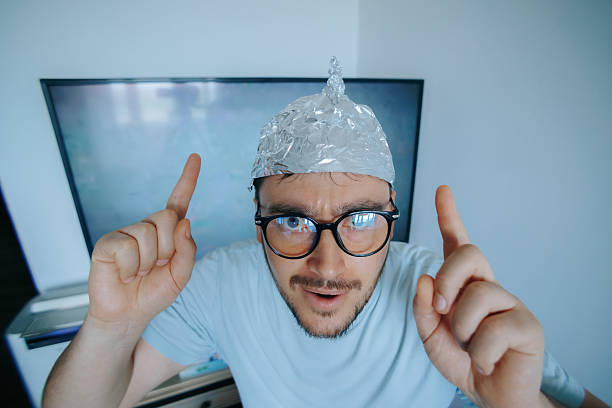 istock Man wearing an aluminum foil hat points upward, expressing paranoia and humor regarding conspiracy theories 2212333786
