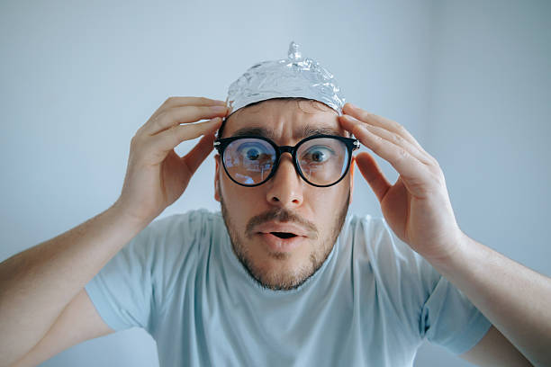 Man wearing an aluminum foil hat expresses disbelief and paranoia while concerned about conspiracy theories