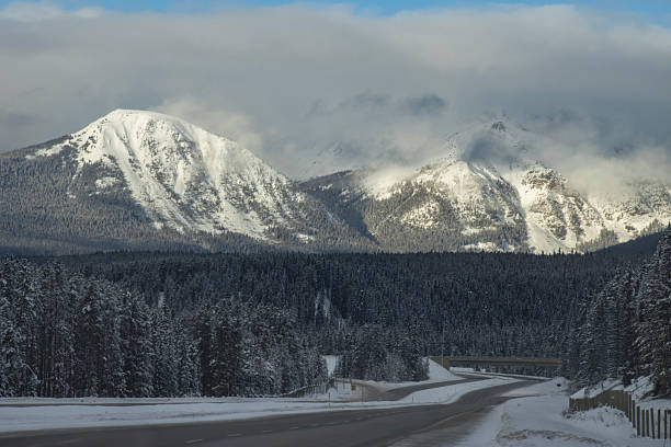istock Snow-covered mountains loom over a winter highway under a cloudy sky in a remote area 2212335131