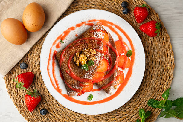 Chocolate crepes filled with strawberries and fruit sauce. Top view.