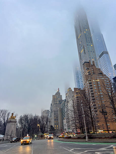 Tall skyscrapers obscured by fog with bustling city traffic below. Urban winter scene with iconic architecture. City streets alive with motion on a cloudy day.