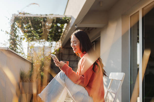 Beautiful Japanese woman using a smartphone while sitting on the balcony