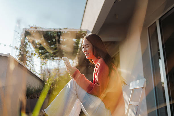 istock Beautiful Japanese woman using a smartphone while sitting on the balcony 2212342102