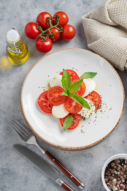 istock Caprese salad with sliced tomatoes, mozzarella and basil on a plate on a light background 2212345735