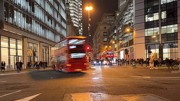 Motion blur of double-decker bus at night, modern skyscrapers line the streets with lights on, London