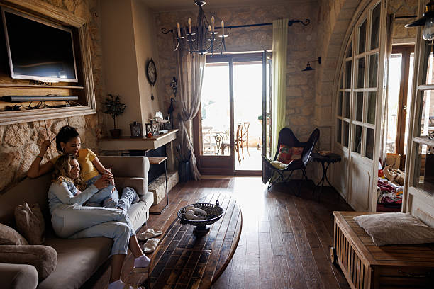 Two young female roommates chilling out at home, sitting on sofa and watching content together on smart phone