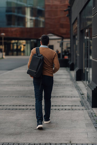 istock Businessman walking down the street with backpack in urban setting 2212358859