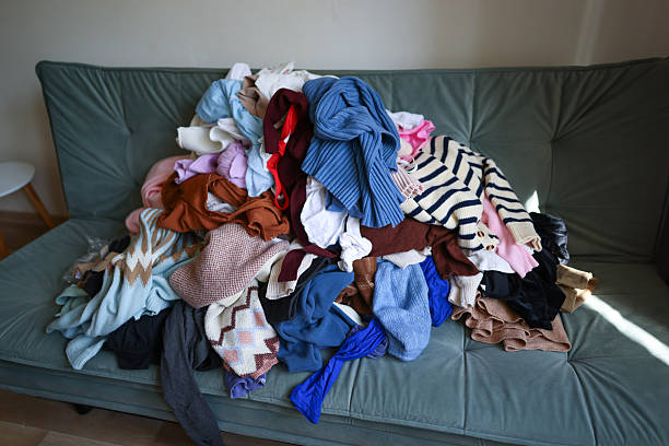 istock Stack of assorted sweaters, shirts, and pants in various colors covering a sofa at home. High quality photo 2212359438