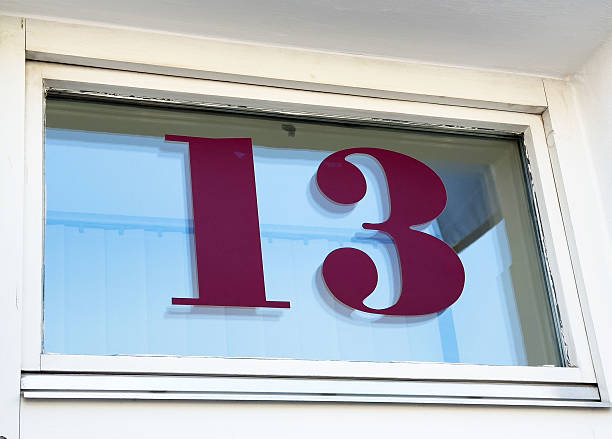 istock Bold burgundy number 13 on glass window reflecting clear blue sky 2212372150
