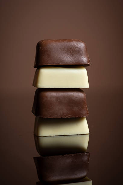 An artful stack of layered chocolates showcasing both dark and white varieties, perfectly balanced to create a visually pleasing display of rich browns and creamy whites.