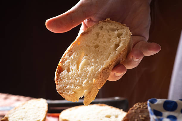 A hand is holding a fresh slice of bread, showcasing its soft and airy texture, with a warm and inviting appearance, perfect for a delicious and satisfying meal.