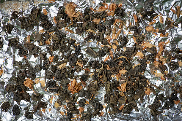 A collection of loose green tea leaves are casually scattered across a reflective aluminum foil sheet. Each curled leaf brings a sense of natural freshness and earthy aroma.